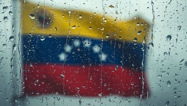 Venezuelan flag fluttering outside window through rain-splattered glass, blurred droplets