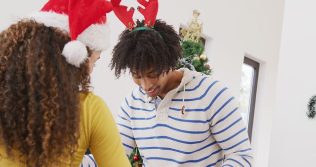 Image of happy diverse couple in reindeer antlers and santa hat dancing by christmas tree at home - Download Free Stock Photos Pikwizard.com