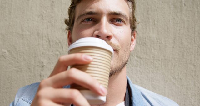Young Man Enjoying Coffee Outdoors Against Wall - Download Free Stock Images Pikwizard.com