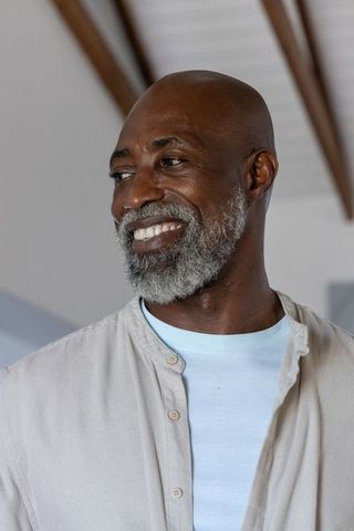 Mature african man smiling at home with vaulted timber rafters, casual beige shirt