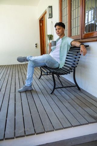 Relaxing Hispanic Man Sitting with Coffee on Porch Bench