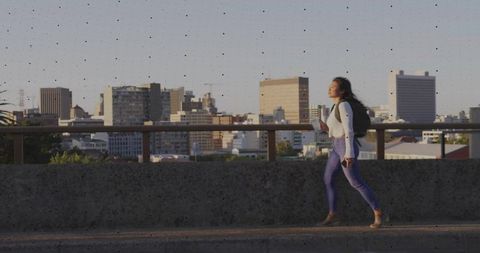 Young Woman with Backpack Walking in City Against Skyline