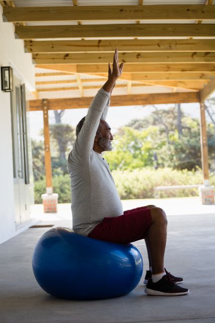 Active senior man exercising on exercise ball in the porch