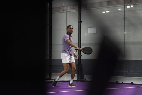 Male athlete playing padel on purple indoor glass court holding paddle ready to strike