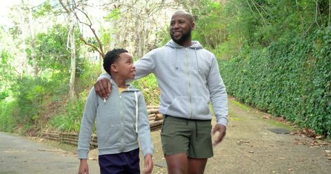 African american father and son walking and bonding on sunlit woodland trail