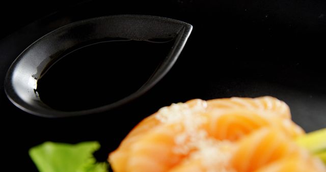 A close-up of a soy sauce dish next to a beautifully presented salmon sashimi on a black background, with copy space. Soy sauce is a staple condiment in Asian cuisine, often paired with sushi and sashimi for an enhanced flavor experience.