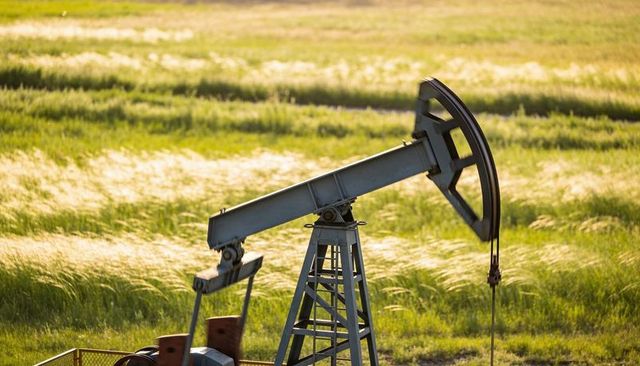 Weathered pumpjack pumping oil across golden prairie grassland at golden hour with walking beam