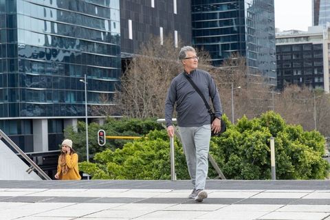 Senior man walking across downtown plaza with messenger bag among glass office towers