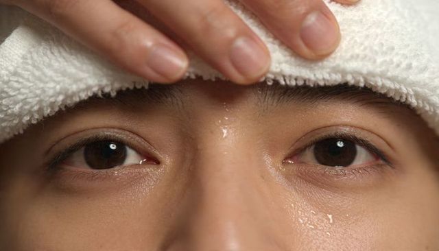 Woman holding white terry towel on forehead showing wet eyes and dewy skin detail