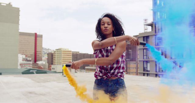 Young biracial woman plays with colorful smoke on a rooftop, with copy space. Casual outdoor fun captures the vibrant energy of youth and urban culture.