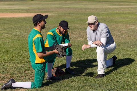 Baseball coach mentoring young players kneeling on grass field during team practice