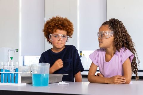 Two african american kids wearing safety goggles doing science experiment with blue liquid