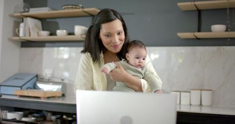Mother with baby engaging with laptop in contemporary kitchen