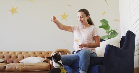 Young woman training happy black-and-white dog in cozy living room