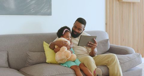 Father and Daughter Bonding on Sofa with Tablet and Teddy Bear