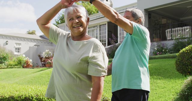 Image of happy biracial senior couple holding hands and dancing in garden. active retirement lifestyle, senior relationship and spending time together concept.