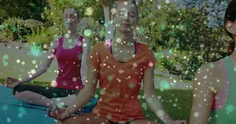 Women meditating outdoors on yoga mats in sunlit garden with sparkling bokeh effects