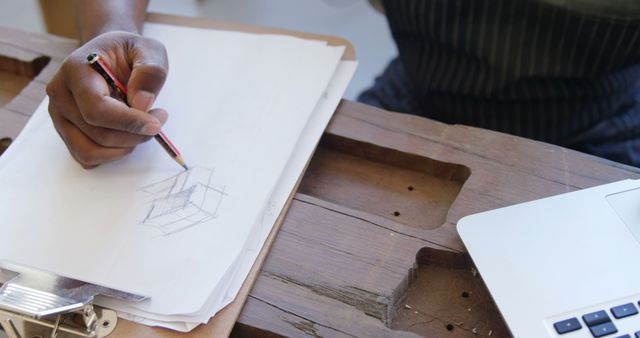 Artist sketches a concept on paper at a wooden desk, with copy space. Creativity flows in this home studio setting with tools of the trade at hand.