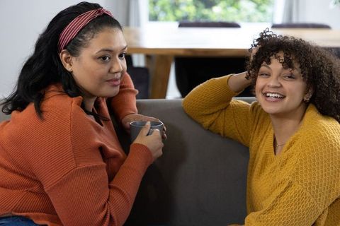 Cozy friendly conversation between diverse female friends on sofa wearing autumn knit sweaters