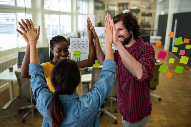 Group of graphic designers giving high five to each other in office