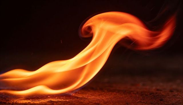 Sweeping ribbon flame curling over pavement with glowing embers and heat ripples