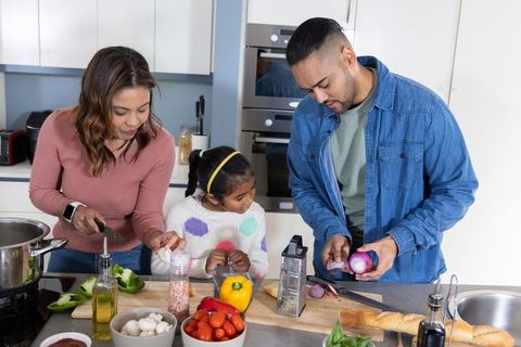 Family cooking together at kitchen island chopping fresh vegetables and preparing meal