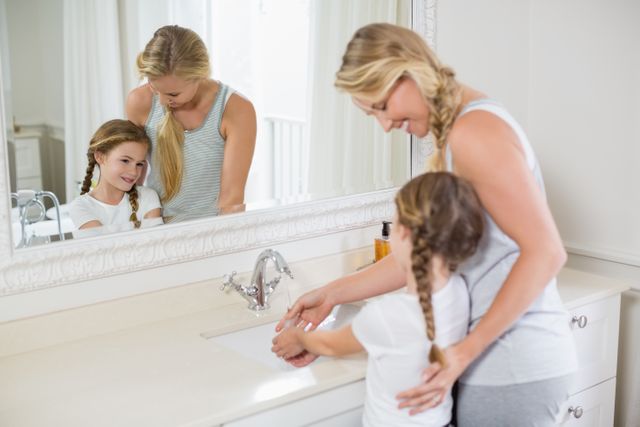 Mother and daughter washing hands together in bathroom, promoting hygiene and family bonding. Ideal for use in parenting blogs, health and hygiene campaigns, family lifestyle articles, and advertisements focusing on cleanliness and family care.
