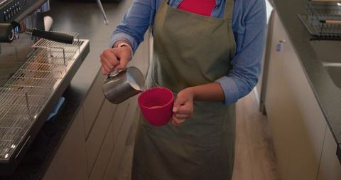 Barista pouring steamed milk into red mug creating latte art at modern coffee counter