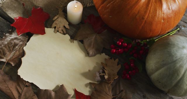 Paper with copy space against autumn leaves, candle and pumpkins on wooden surface. halloween festivity and celebration concept