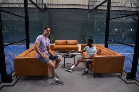 Post-match athletes relaxing on leather sofas in industrial sports lounge reaching for water