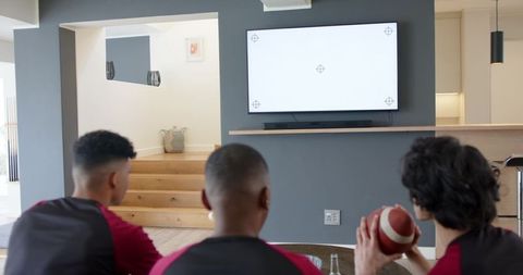 Diverse teammates watching tv calibration holding football in modern open-plan lounge