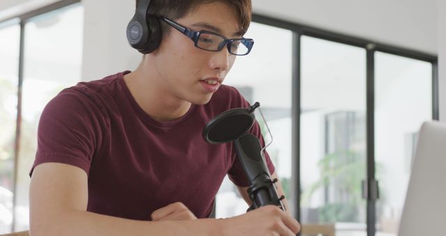 Asian boy wearing headphones speaking on professional microphone to record audio podcast at home. teenager lifestyle and living concept