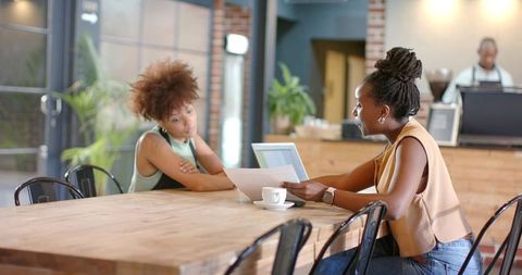 Discussing paperwork over laptop at contemporary cafe table, casual business meeting