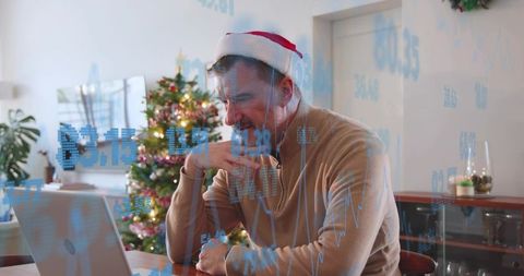 Trader wearing santa hat analyzing financial charts on laptop at home during holidays