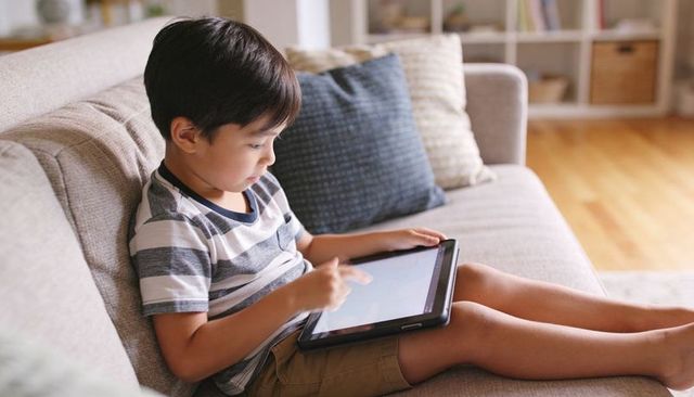 Young boy using tablet on sofa for digital learning and play in sunlit modern living room