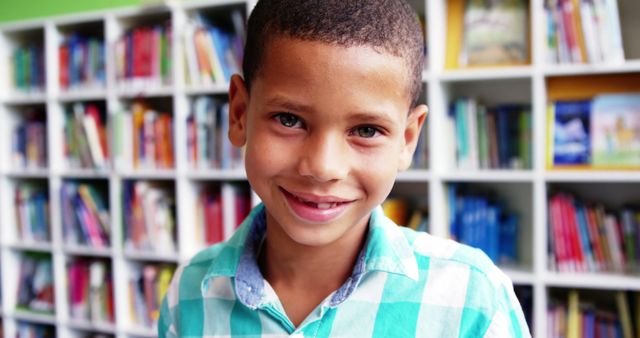 Young boy with a pleasant smile standing in front of bookshelves in a library. Great for educational content, promotional materials for schools or libraries, reading programs, or advertisements highlighting children's happiness and love for learning.