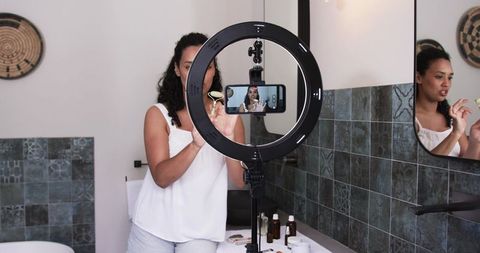 Recording skincare tutorial with ring light and smartphone in modern bathroom mirror