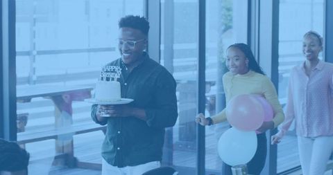 Colleague carrying birthday cake while teammates bringing balloons in bright office
