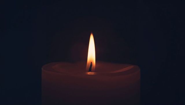 Pillar candle casting warm halo on dark background minimalist close-up