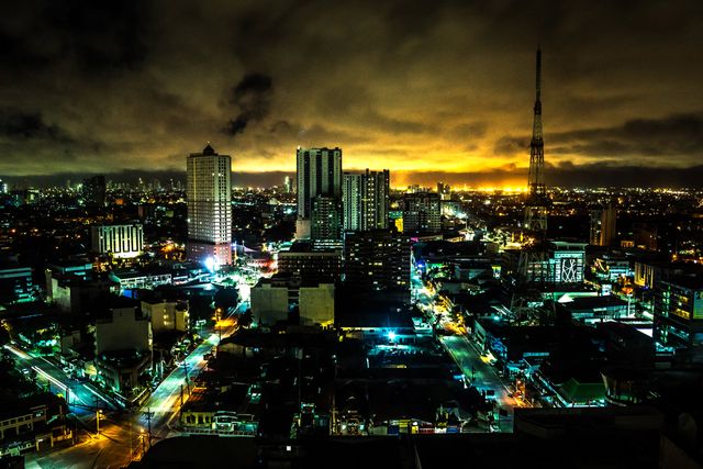Photo showcases an urban skyline at night with high-rise buildings and brightly lit streets. The dramatic sky adds an intense atmosphere. Ideal for use in urban lifestyle blogs, travel websites, marketing materials for city real estate, and backgrounds for digital presentations or creative projects highlighting urban life.