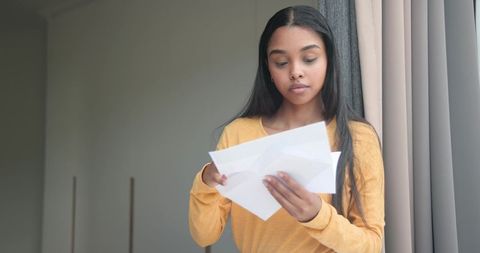 Young woman reading mail by window with curtains and soft sunlight, home interior