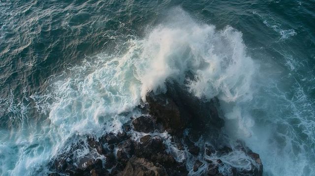 Aerial crashing waves striking jagged coastal rocks turquoise foam spraying teal seascape
