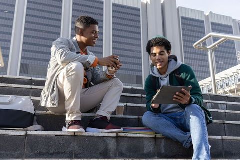 College Friends Studying Outdoors on Campus Steps Using Tablet and Notebooks
