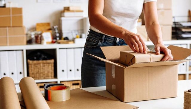 Small Business Owner Packing Handmade Parcel into Cardboard Box at Home Fulfillment Station