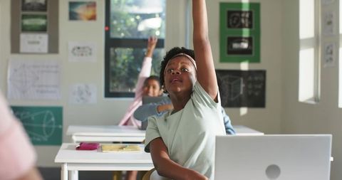 African american preteen raising hand in classroom with laptop and geometry posters
