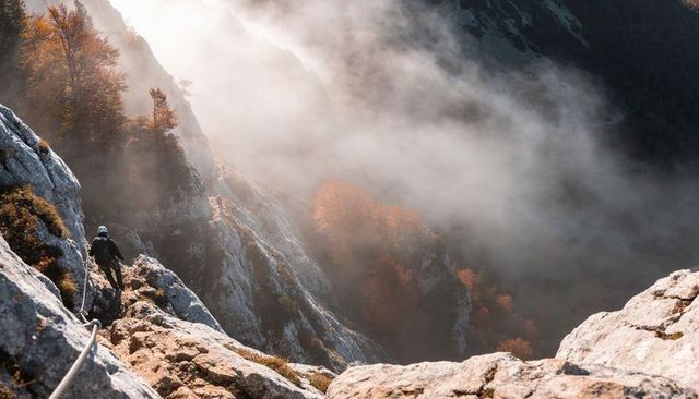 Helmeted climber traversing misty alpine ridge sunrise clipping into ferrata safety cable