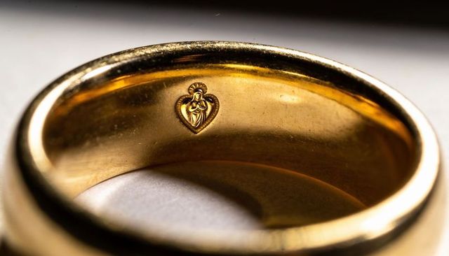 Gold wedding band showing heart hallmark and worn patina macro detail on polished interior