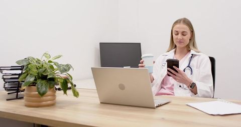 Female physician using smartphone and laptop in modern clinic office