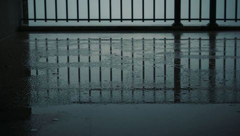 Reflecting metal railing on wet balcony floor creating repeating baluster puddle reflections