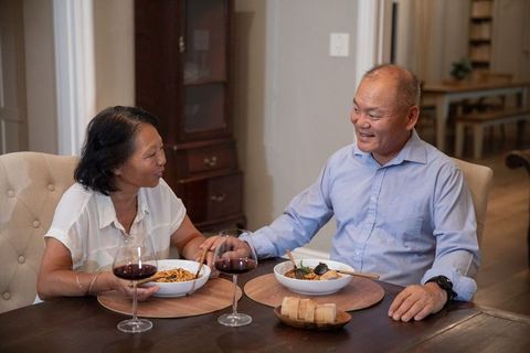 Asian couple enjoying intimate home dinner sharing noodle bowls and red wine glasses